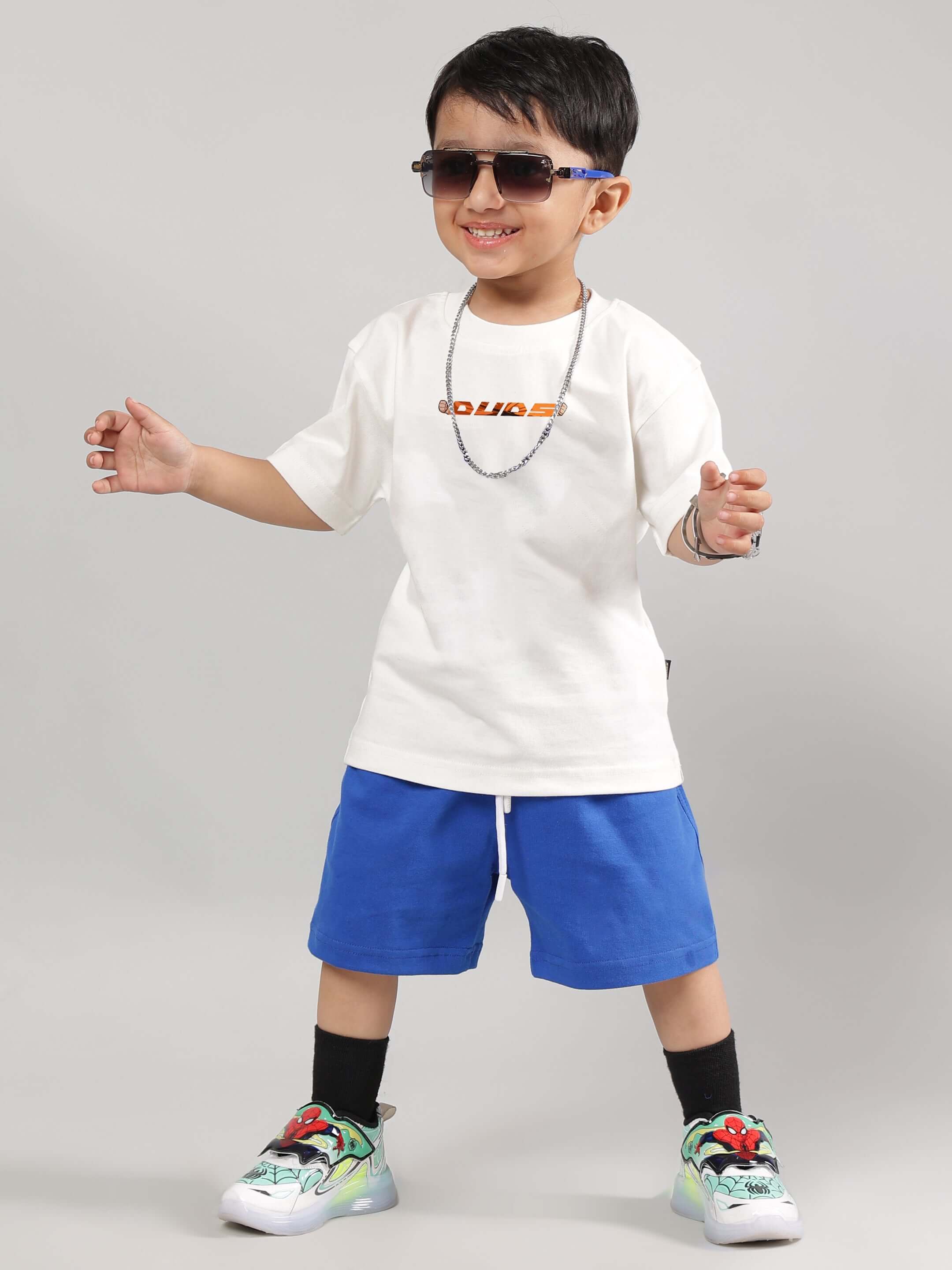 Child wearing off-white GOHAN t-shirt paired with blue shorts and colorful sneakers, showcasing casual kid's fashion by DUDS.
