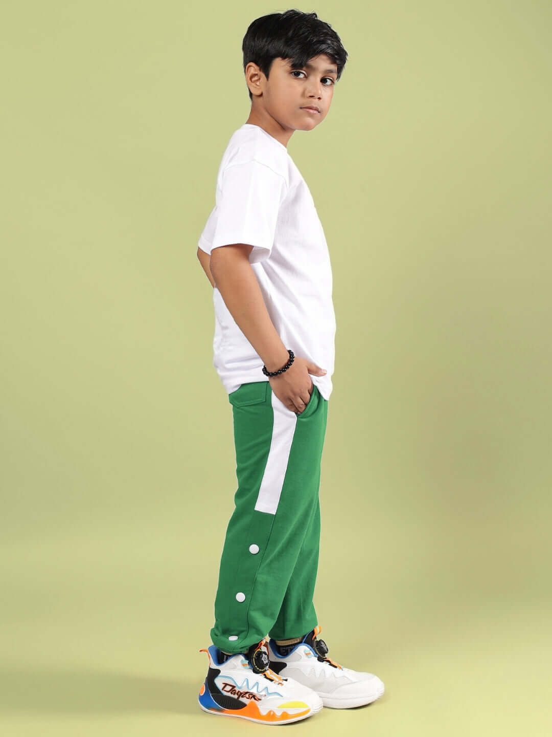 Boy wearing Goku and Bulma printed white-green co-ord set with green pants and a white t-shirt, standing sideways on a light green background.
