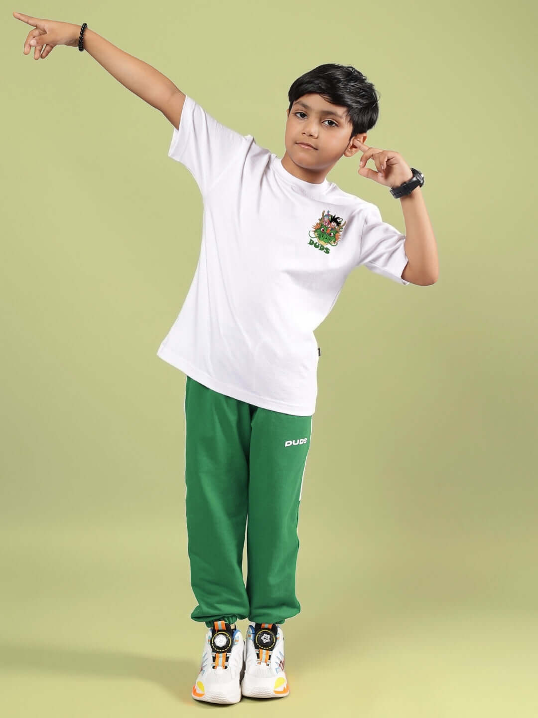 Child wearing GOKU AND BULMA PRINTED T-SHIRT FOR BOYS GIRLS WHITE with green pants, playful pose