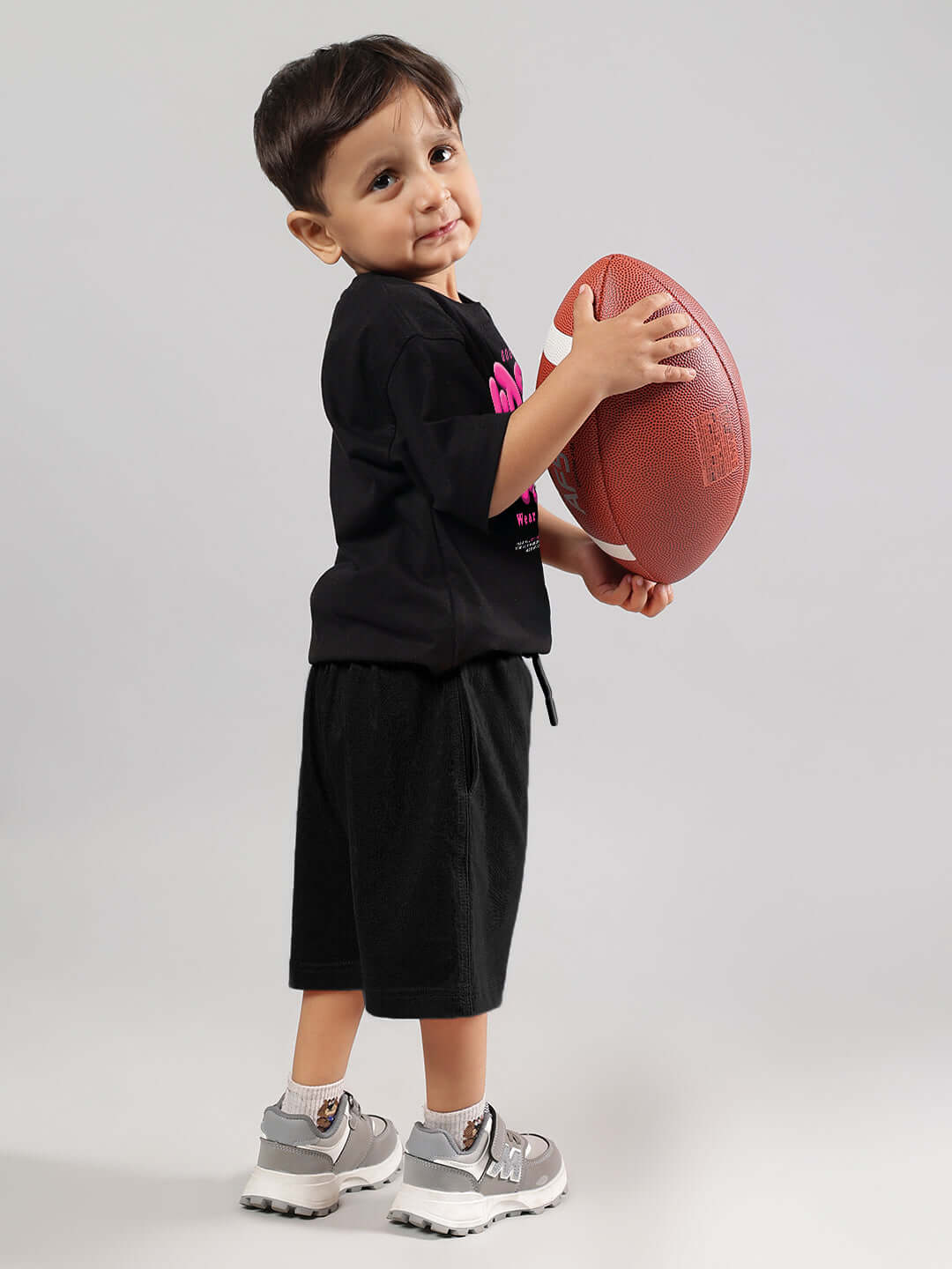 Alt Tag: Child wearing a black Good Vibes T-shirt holding a football, promoting versatile kids' fashion by DUDS.