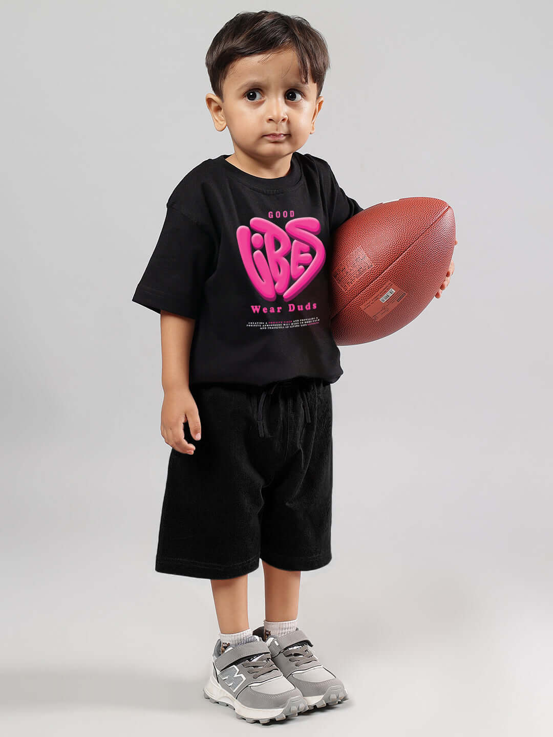 Child wearing GOOD VIBES CO-ORD FOR BOYS GIRLS BLACK-ORANGE holding a football, showcasing trendy kids' outfit with pink logo.
