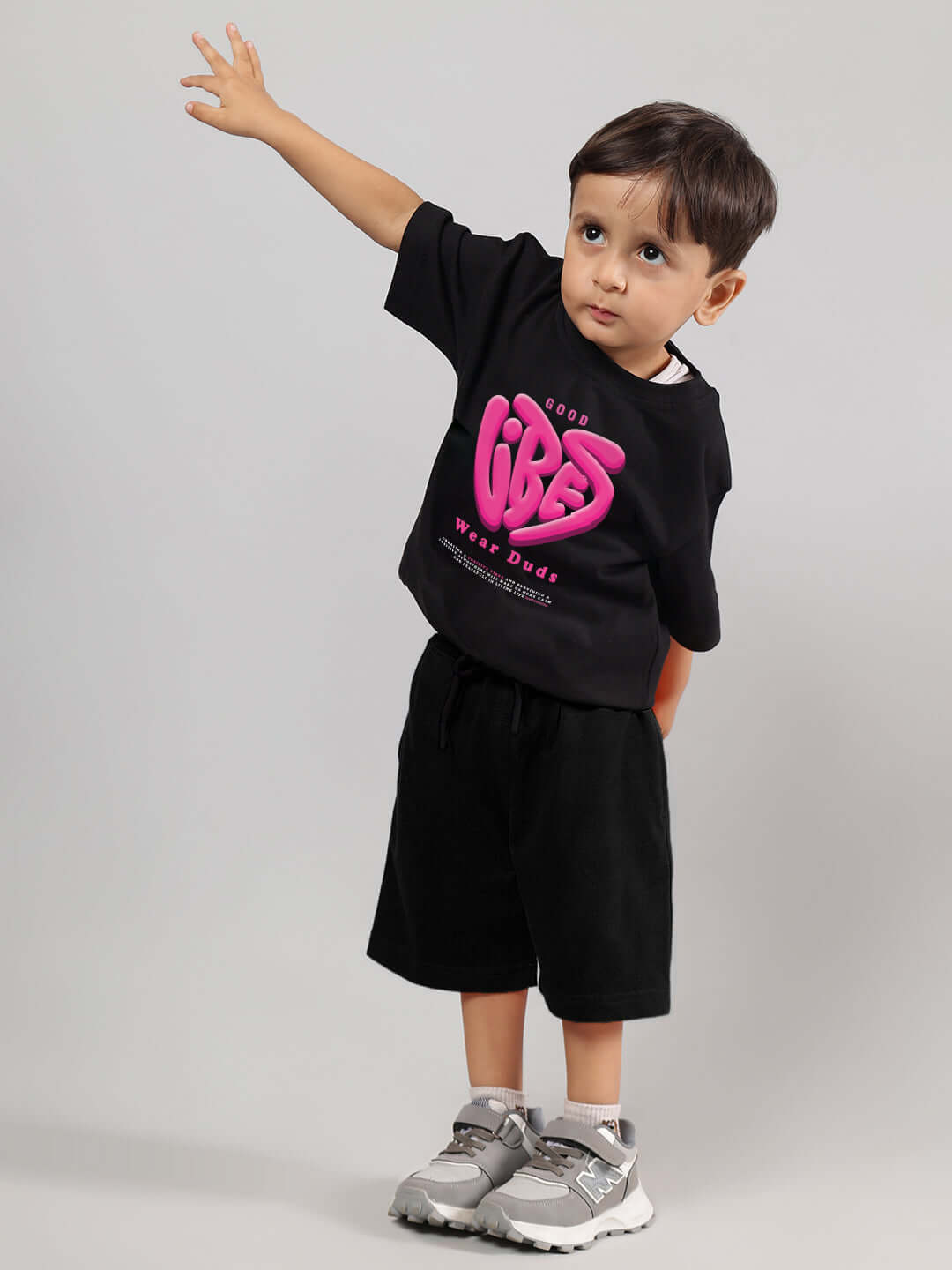 Child wearing GOOD VIBES CO-ORD FOR BOYS GIRLS BLACK-ORANGE, featuring black top with vibrant design, matching shorts, and gray sneakers.
