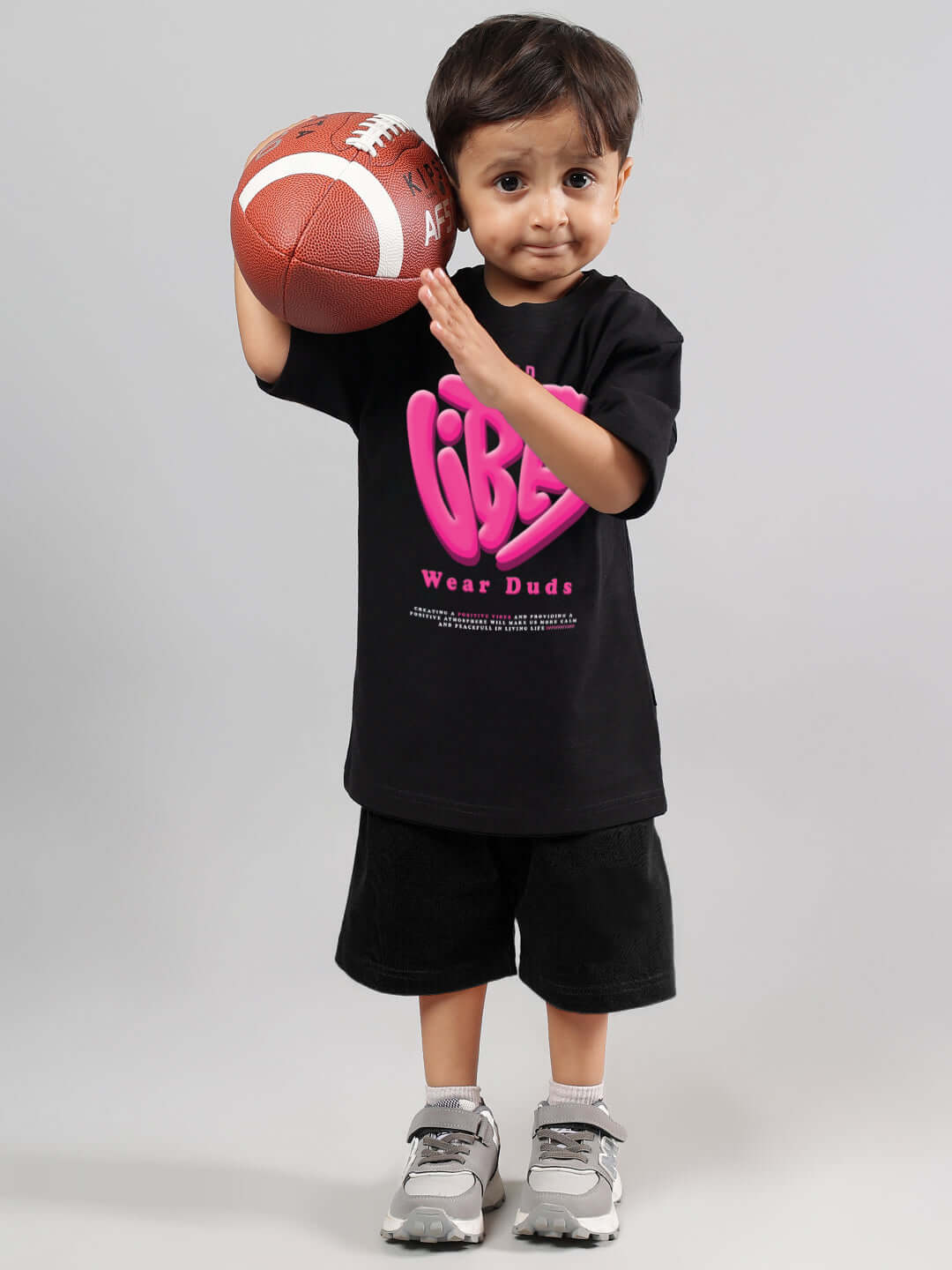 Child holding a football wearing a black 'Good Vibes' T-shirt, designed for boys and girls by DUDS, showcasing sporty fashion.