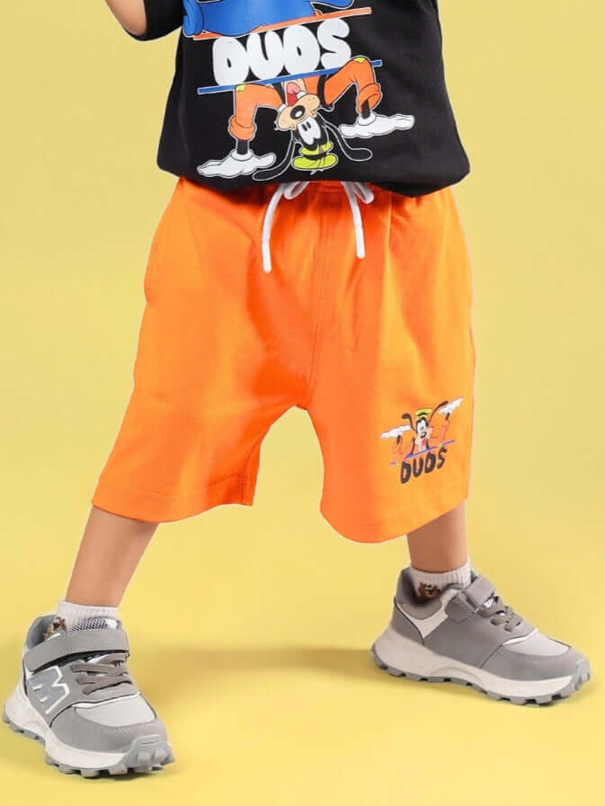 Child wearing orange Goofy shorts from DUDS, perfect for boys and girls, shown with a playful cartoon design on a yellow background.