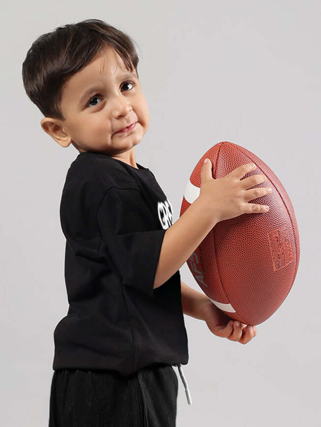 Child in black oversized t-shirt holding a football, showcasing the Great Printed T-Shirt for Boys & Girls.