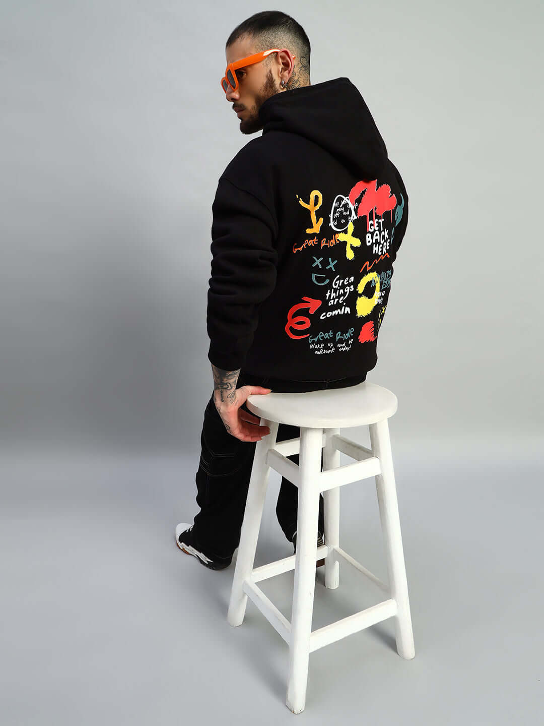 Person wearing Great Ride Oversized Fleece Hoodie Black with colorful graphic design, sitting on a white stool.