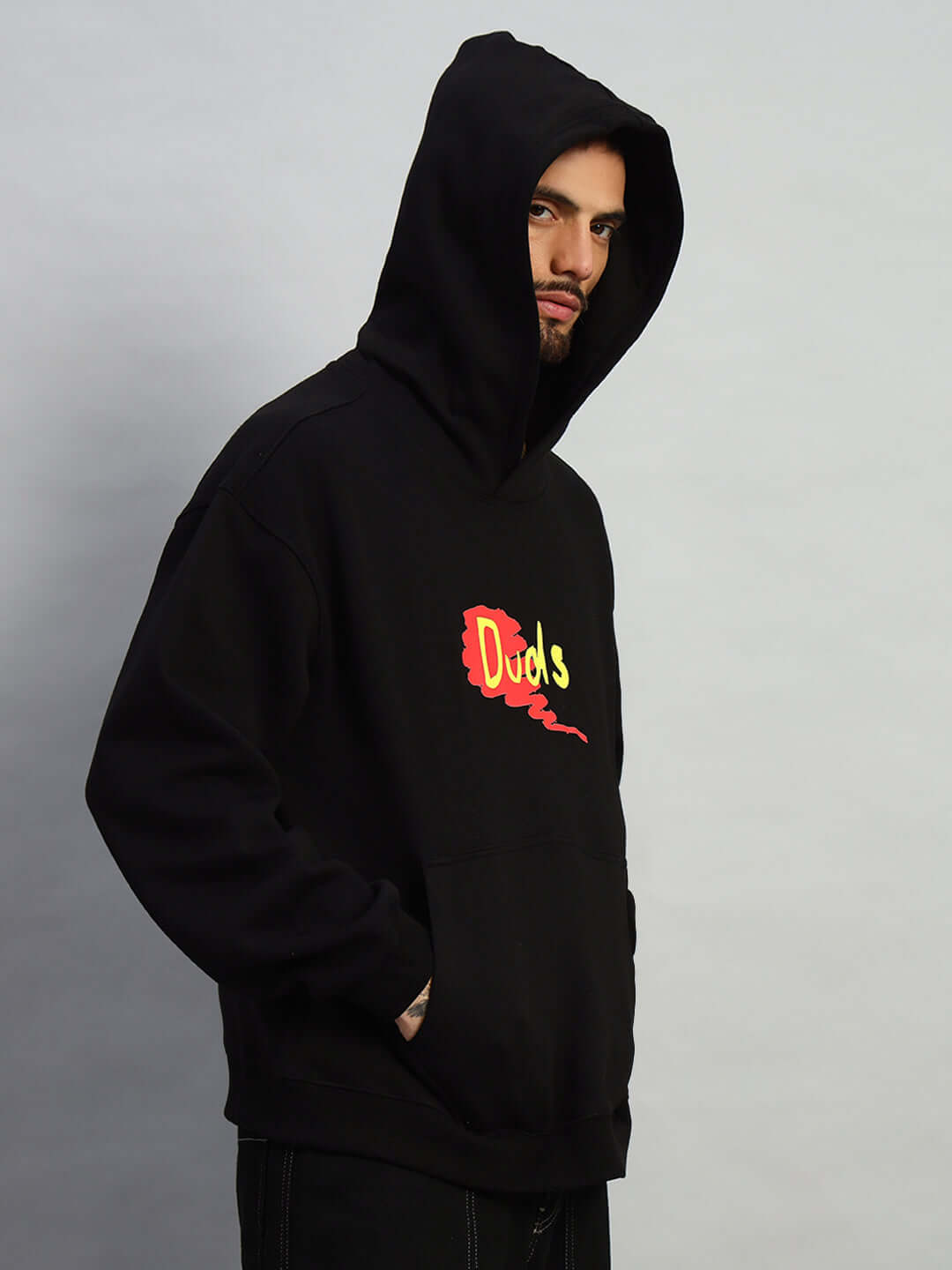 Model wearing Great Ride oversized black fleece hoodie with colorful logo on chest, hands in pockets, facing sideways.