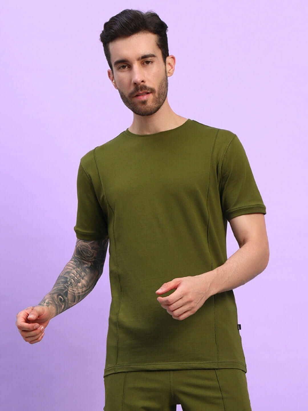 Man wearing GREEBLE REGULAR FIT T-SHIRT OLIVE GREEN on a purple background, showcasing casual style.