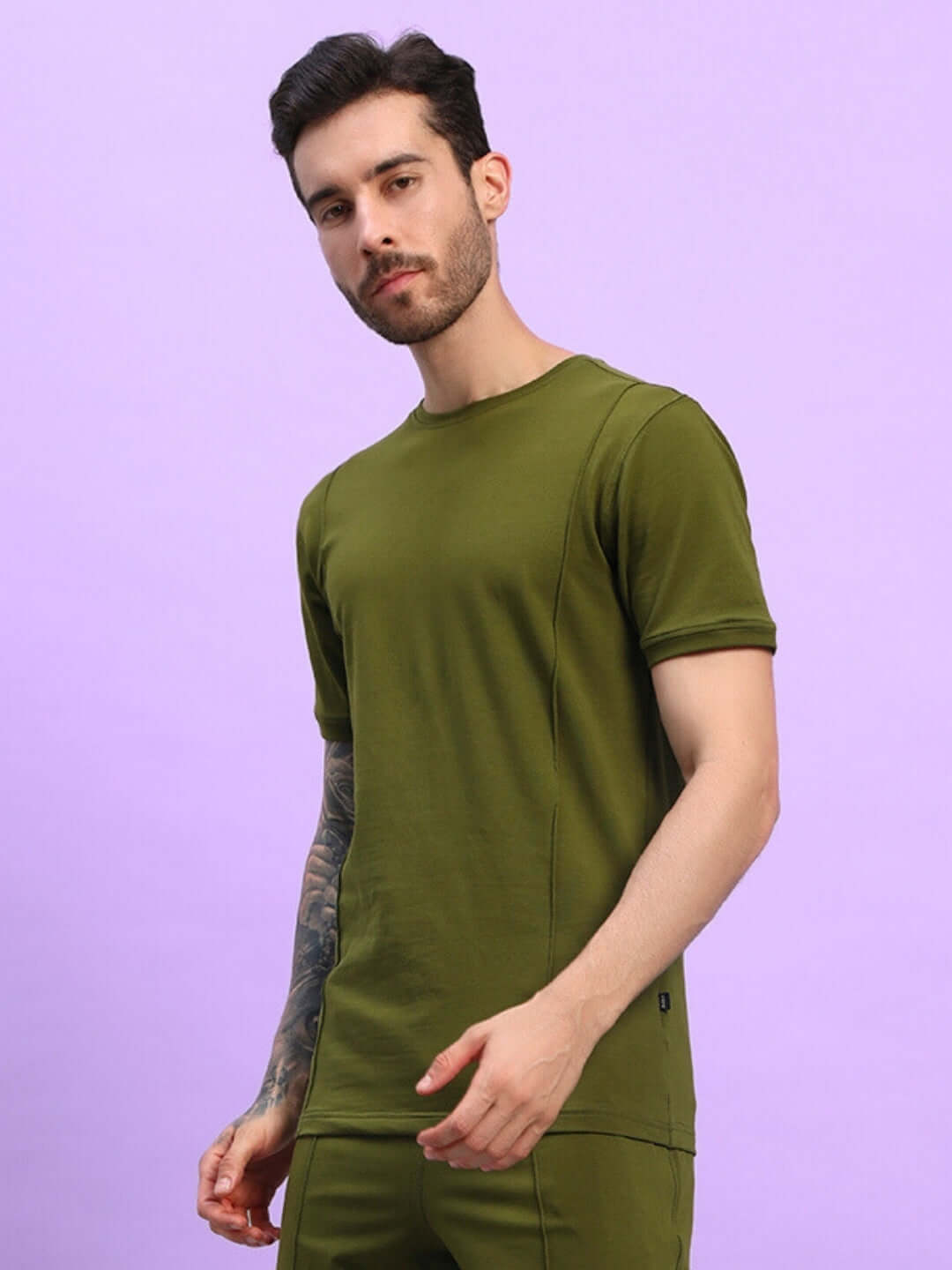 Man wearing GREEBLE REGULAR FIT T-SHIRT OLIVE GREEN against a lavender background, showcasing casual and versatile style.