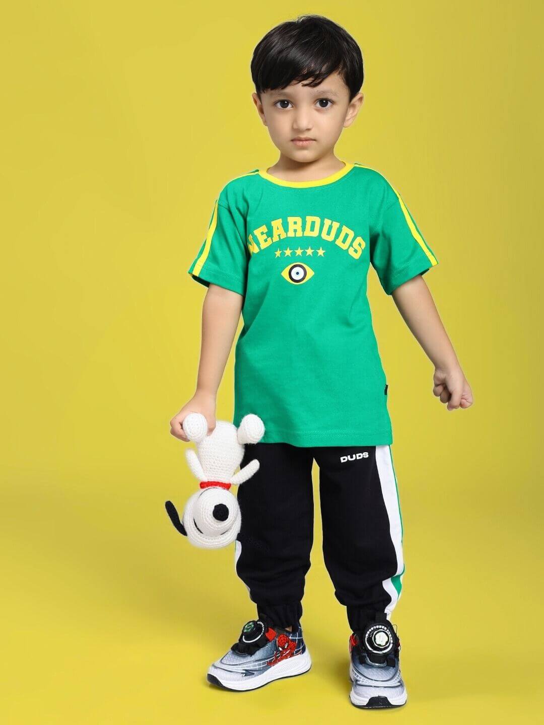 Child wearing an IRISH T-SHIRT FOR BOYS AND GIRLS GREEN holding a plush toy, standing against a yellow background.