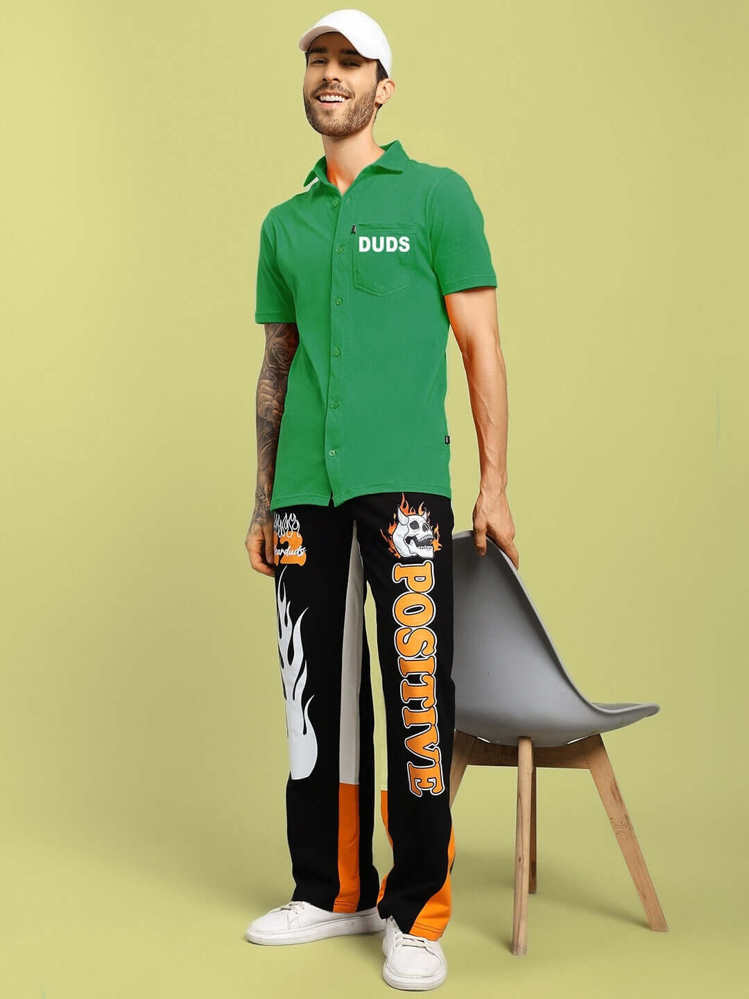 Man wearing green WINGS TEE REGULAR FIT SHIRT by DUDS, standing next to a chair with custom fit pants displaying 'POSITIVE.'