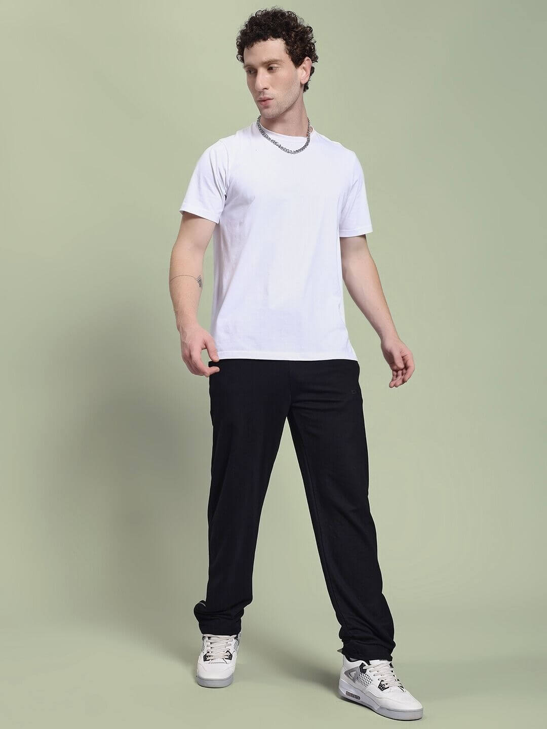Man wearing JOSS WINS RELAXED-FIT JOGGER BLACK and white t-shirt standing against green background.