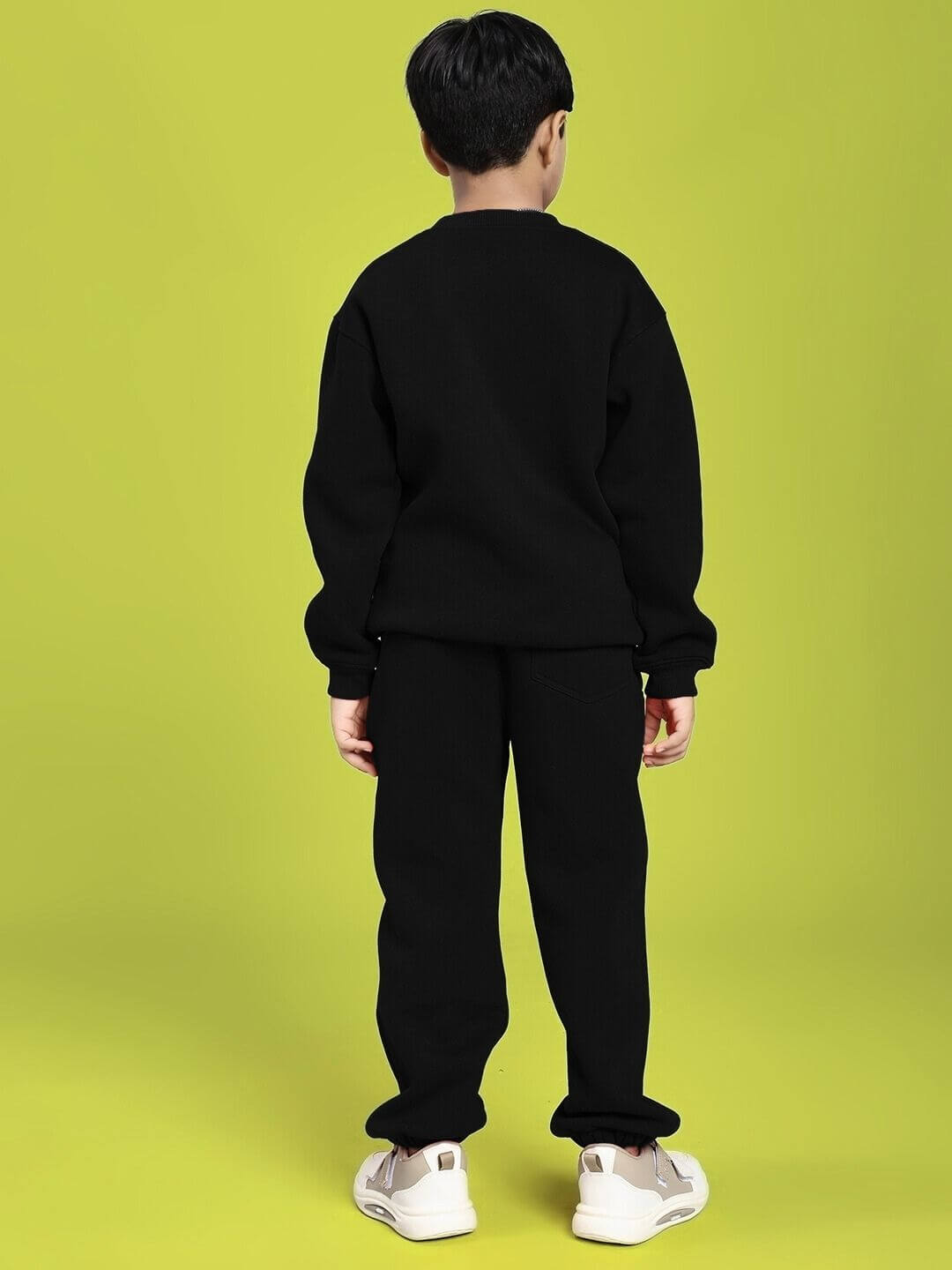 Child wearing GROW AND GLOW PRINT FLEECE CO-ORD FOR BOYS AND GIRLS BLACK, standing against a green background, showcasing the back design.