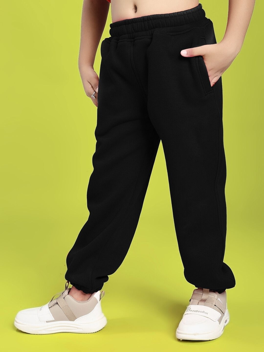 Child wearing GROW AND GLOW PRINT FLEECE CO-ORD FOR BOYS AND GIRLS BLACK with white sneakers on a green background.