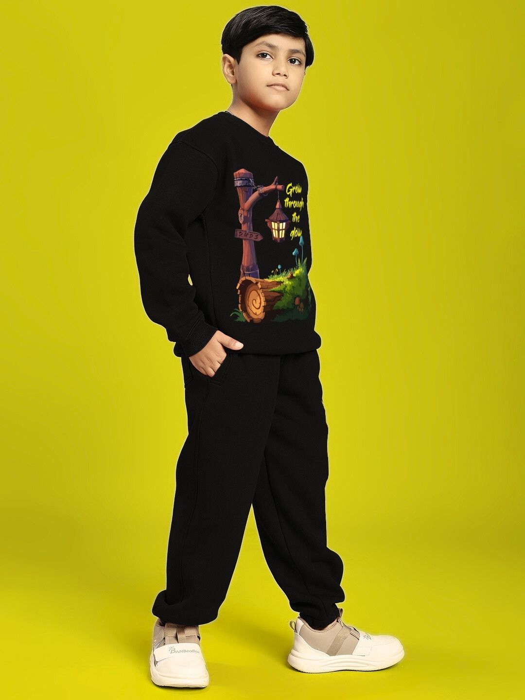 Child wearing GROW AND GLOW PRINT FLEECE CO-ORD FOR BOYS AND GIRLS BLACK, standing confidently against a bright yellow background.