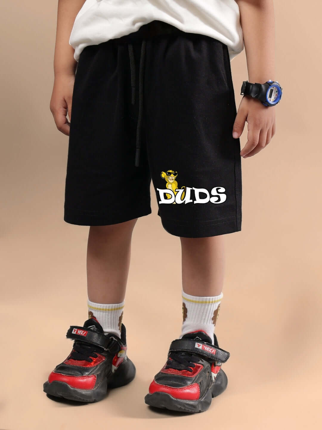Child wearing HAKUNA MATATA SHORTS FOR BOYS & GIRLS BLACK by DUDS, showcasing casual style with red-black sneakers.