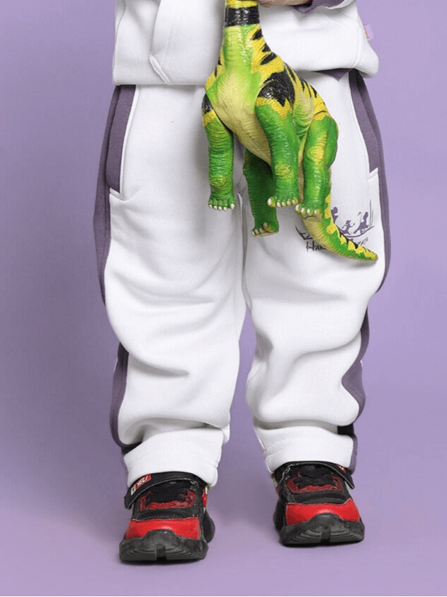 Child wearing Hakuna Matata white-violet fleece pants holding a dinosaur toy.