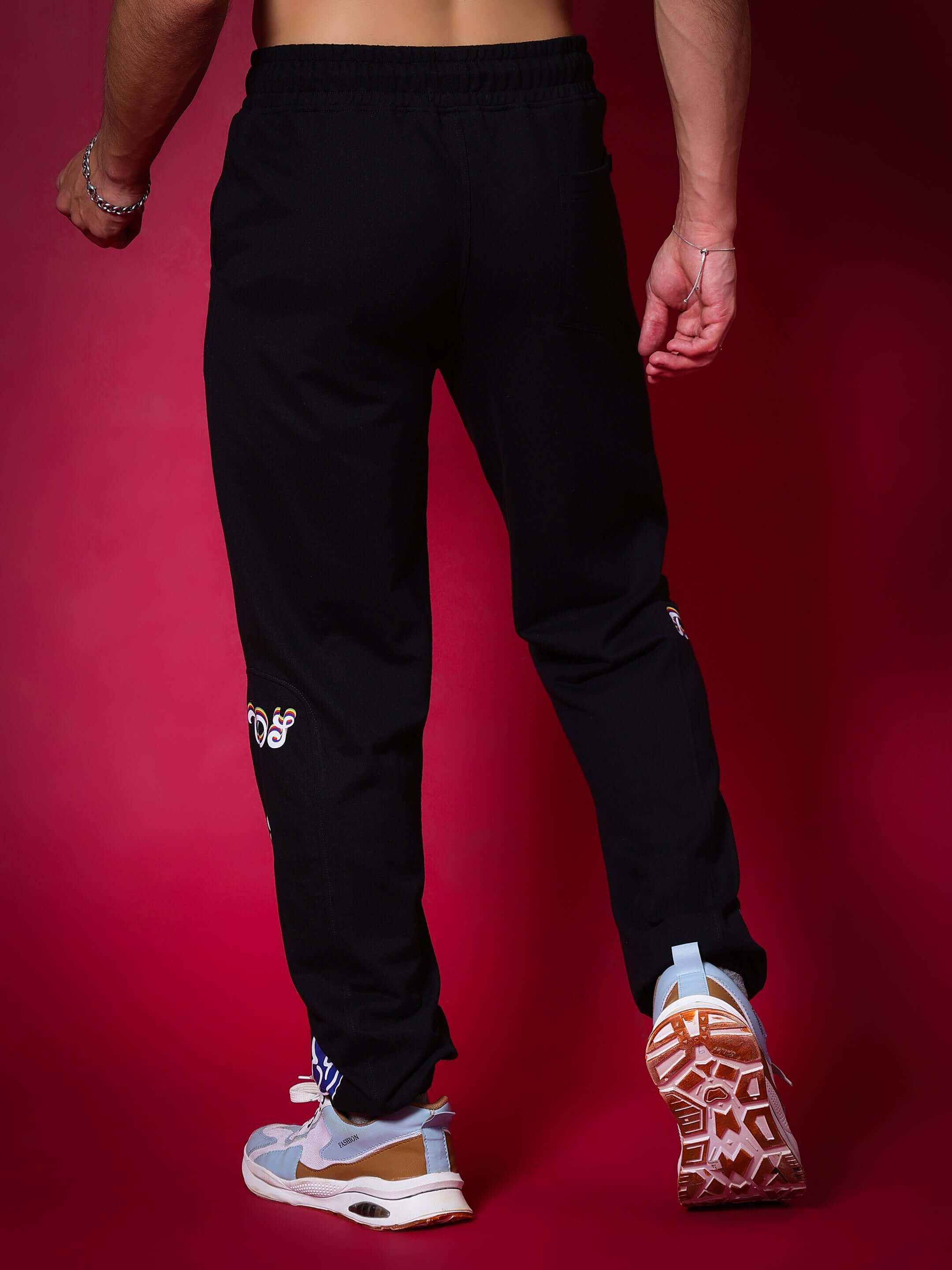 Man wearing black relaxed jogger pants with white sneaker, standing against a red background.