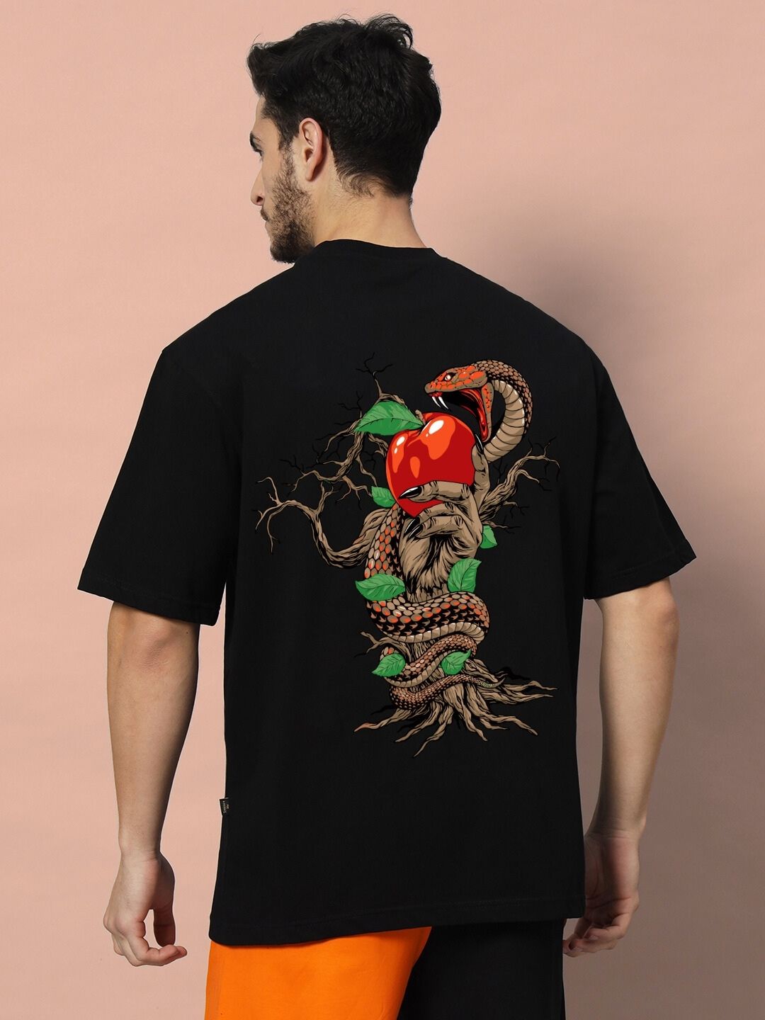 Rear view of HAND SNAKE APPLE OVERSIZED T-SHIRT BLACK, featuring a snake and apple graphic, worn by a man against a peach background.