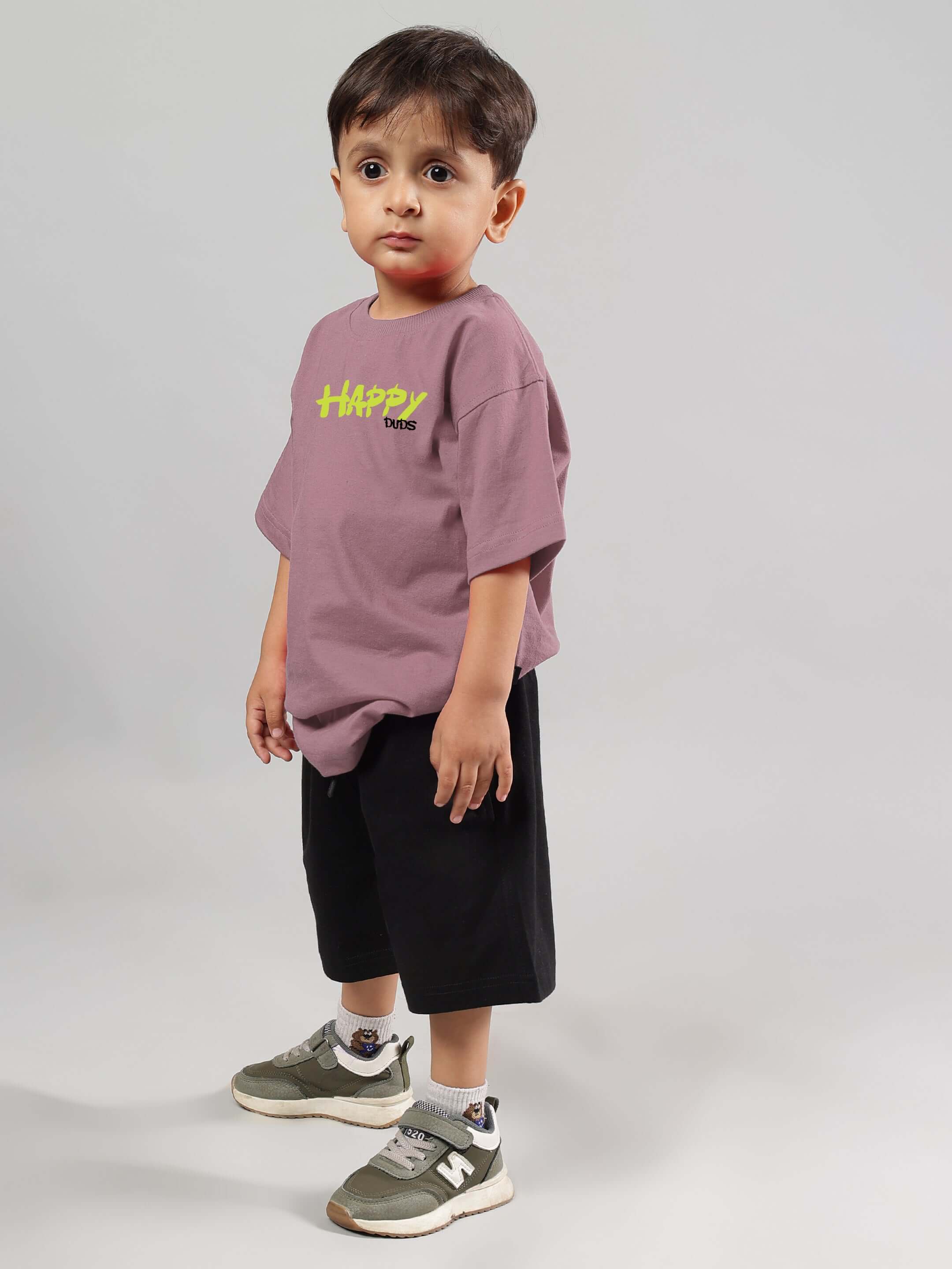 Child wearing a Happy Duds oversized t-shirt in Chinese Violet color, styled with black shorts and sneakers.