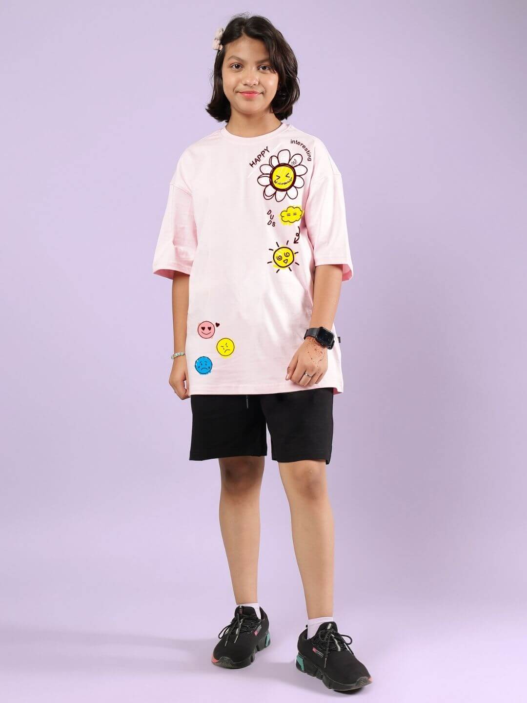 Child wearing a pink-black co-ord set with floral designs, smiling and standing against a purple background.