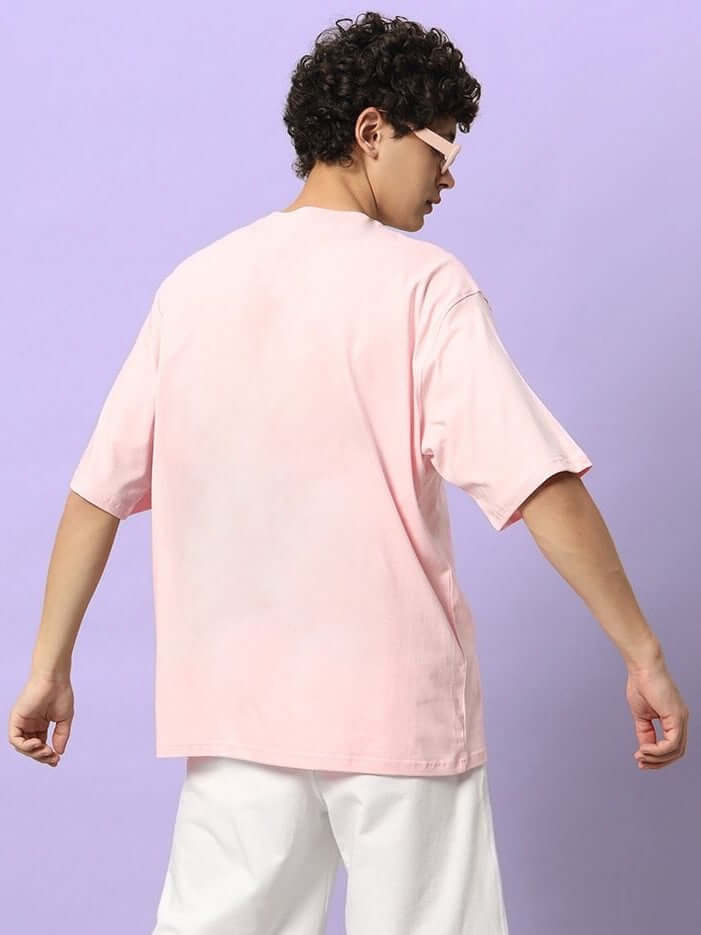 HAPPY INTERESTING OVERSIZED T-SHIRT PINK modeled from the back, showcasing its relaxed streetwear style against a purple background.