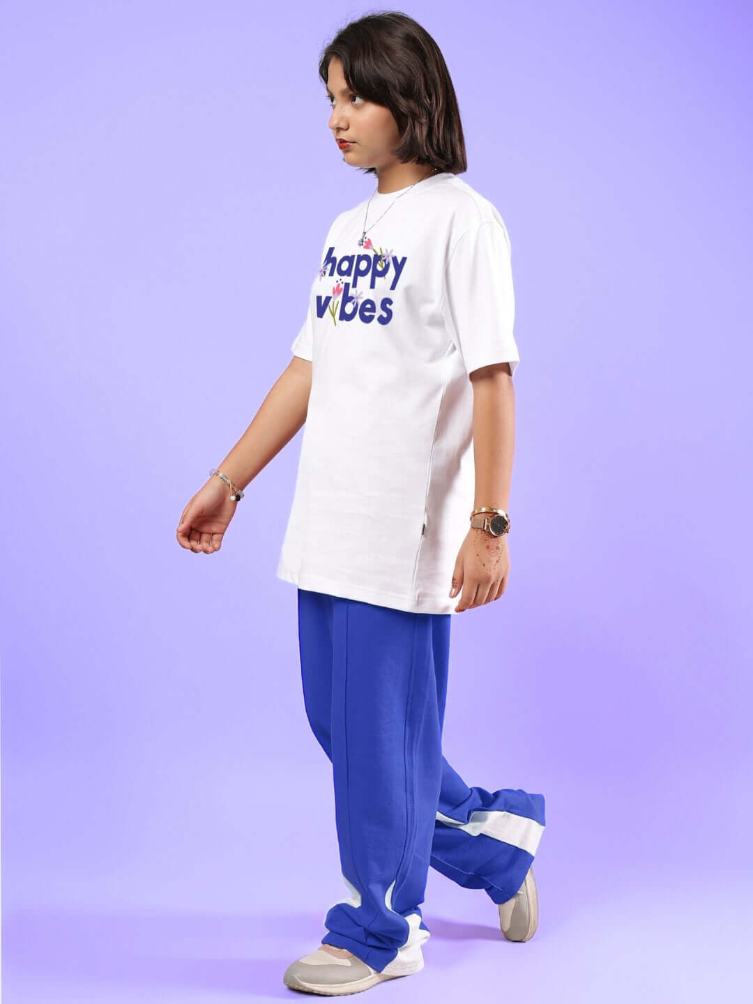 Child wearing Happy Vibes white and blue co-ord set, includes a t-shirt and pants, standing against a purple background.