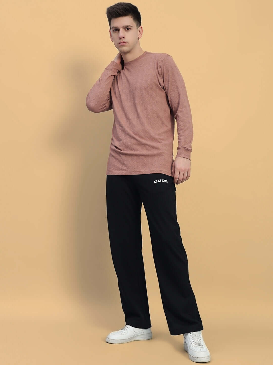 Model wearing HARPER relaxed fit jogger in black, paired with a casual pink shirt and white sneakers on a beige background.