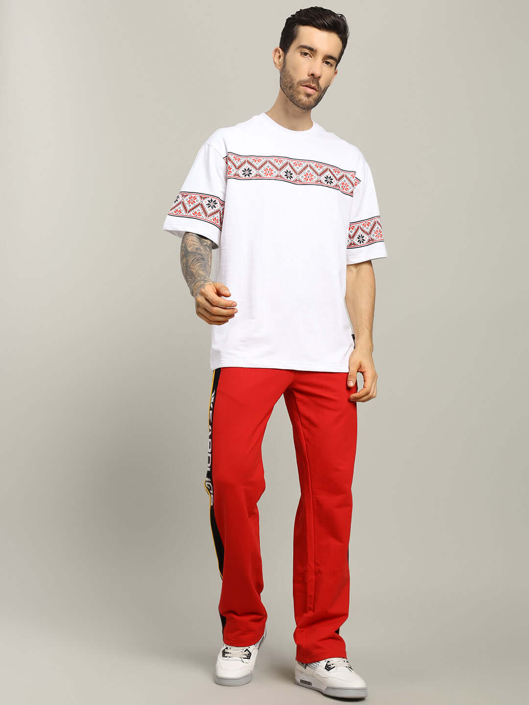 Man wearing HEADPHONES ORNAMENT PRINTED T-SHIRT WHITE with red pants, showcasing cultural and modern streetwear style.