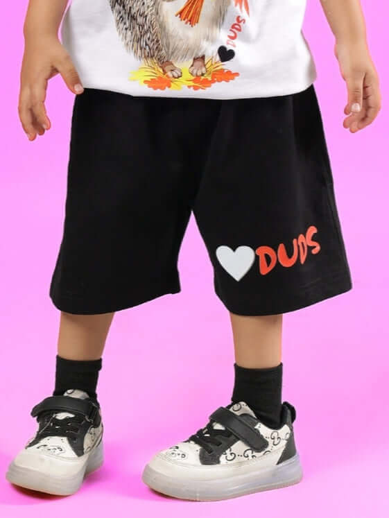 Child wearing HEDGEHOG SHORTS FOR BOYS & GIRLS BLACK with DUDS logo on pink background.
