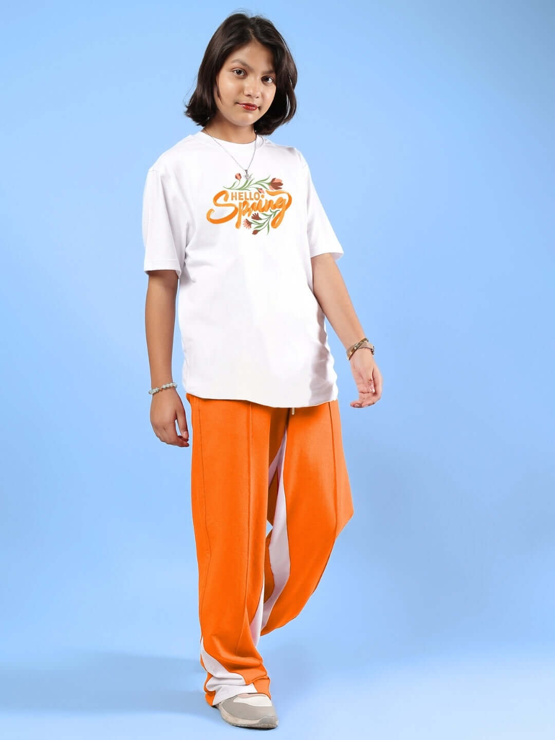 Child wearing HELLO SPRING CO-ORD FOR BOYS & GIRLS WHITE-ORANGE with playful floral design on a light blue background.