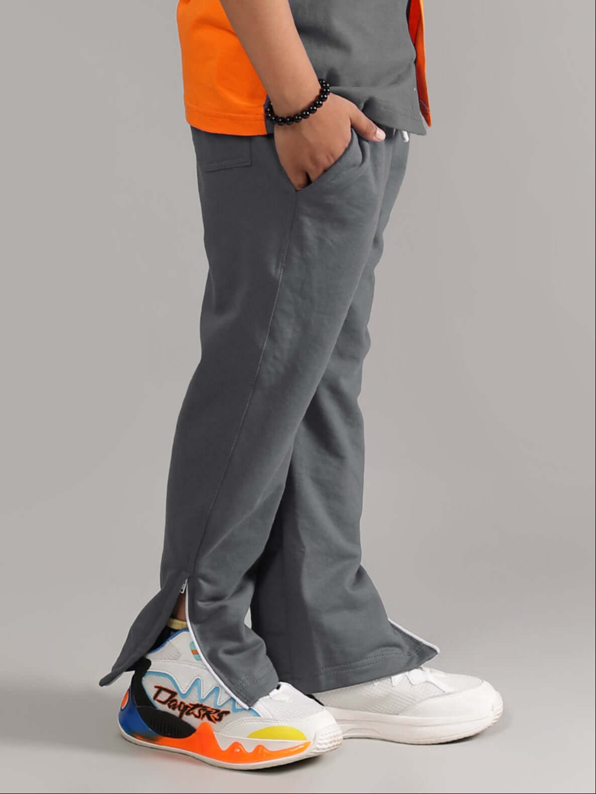 Boy wearing grey HERSHEY JOGGER FOR BOYS & GIRLS GREY with colorful sneakers, side view showcasing relaxed fit and ankle zipper.