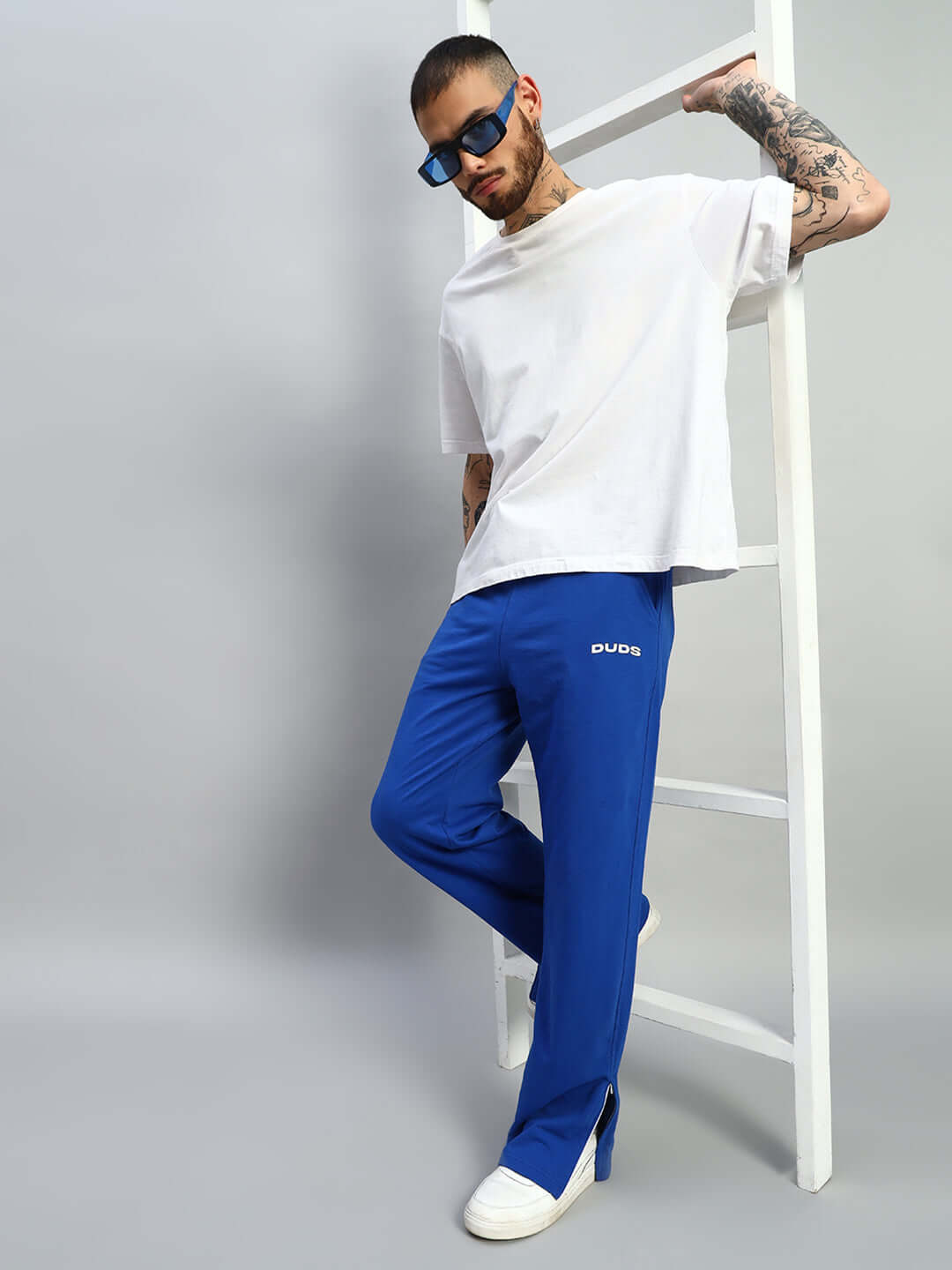 Model wearing royal blue joggers with side slits, paired with a white t-shirt and sunglasses, showcasing DUDS fashionable casual wear.