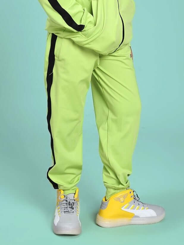 Child wearing HIGH PERFORMANCE JOGGER FOR BOYS AND GIRLS NEON GREEN with sneakers on a teal background.