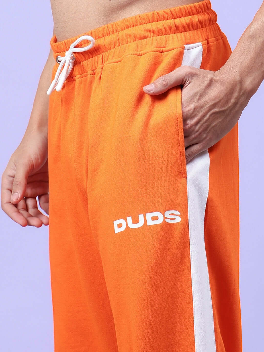 Model wearing HIGH POINT CONTRAST JOGGERS in orange-white with DUDS logo, showcasing elastic waistband and side pocket detail.