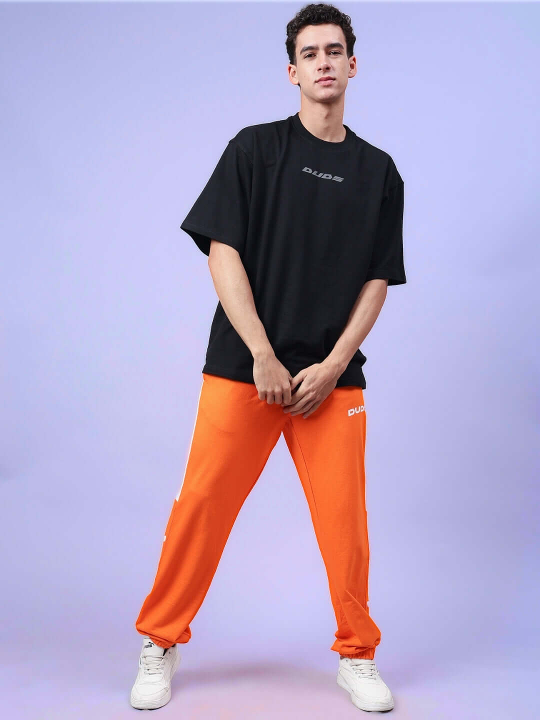 Model wearing DUDS High Point Contrast Joggers in orange-white, styled with a black t-shirt and white sneakers.