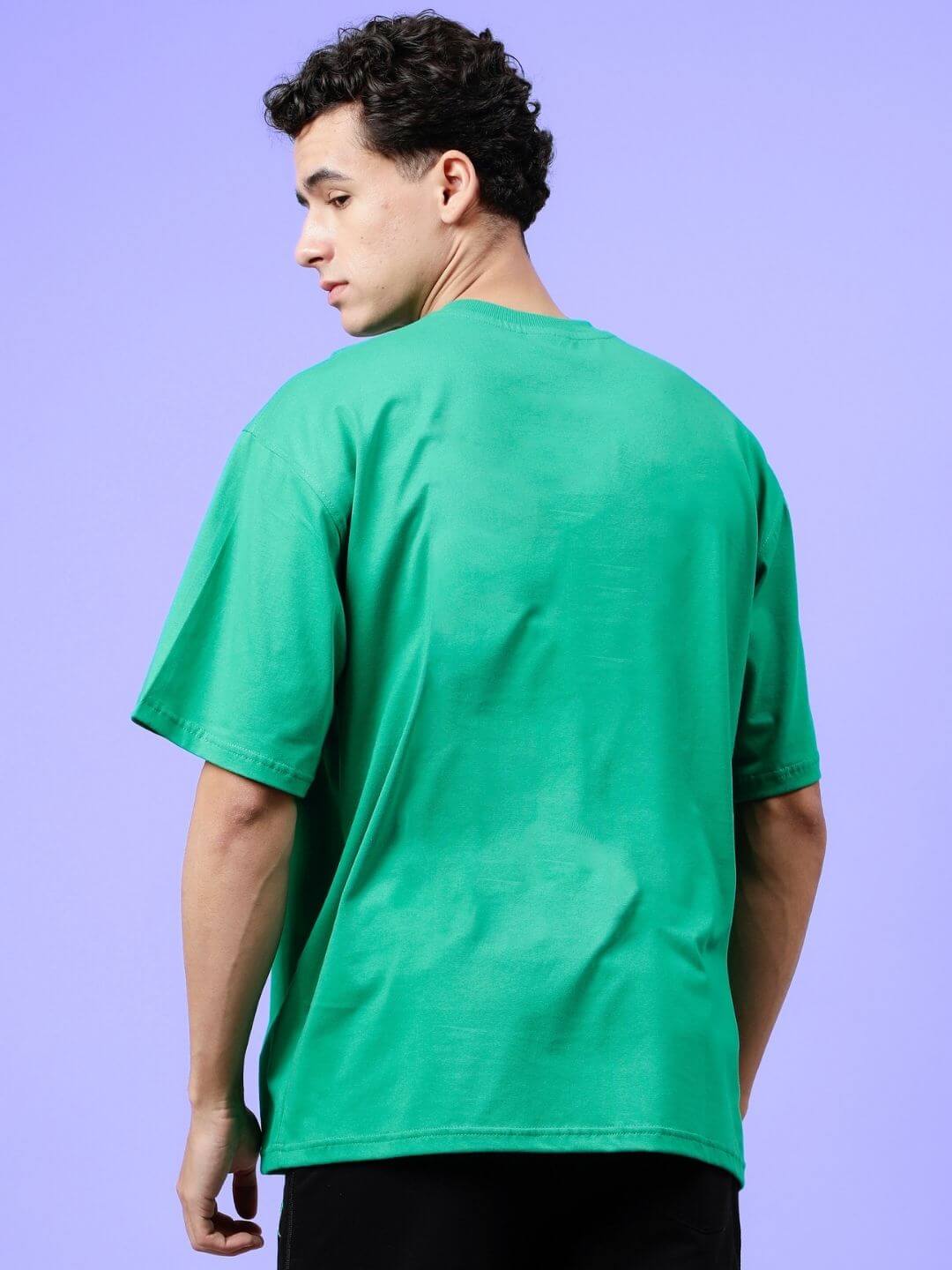 Back view of model wearing HIP HOP OVER-SIZED T-SHIRT GREEN, showcasing relaxed fit and vibrant color against a purple background.