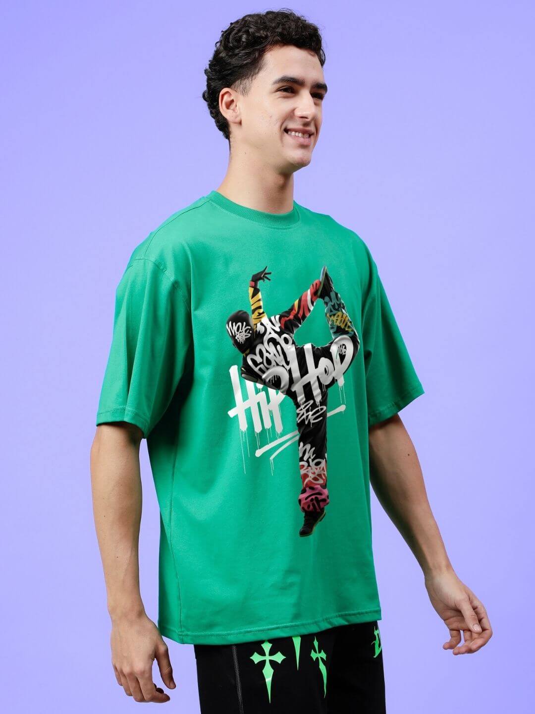 Man wearing HIP HOP OVER-SIZED T-SHIRT GREEN, showcasing streetwear with bold graphics on purple background.