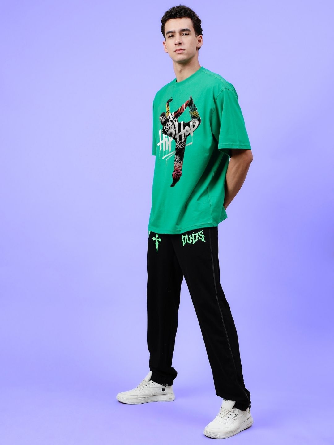 Model wearing HIP HOP OVER-SIZED T-SHIRT GREEN paired with black pants against a purple background.