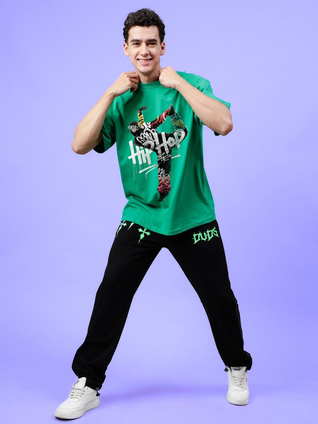 Man wearing HIP HOP OVER-SIZED T-SHIRT GREEN showcasing streetwear style with a vibrant design against a purple background.