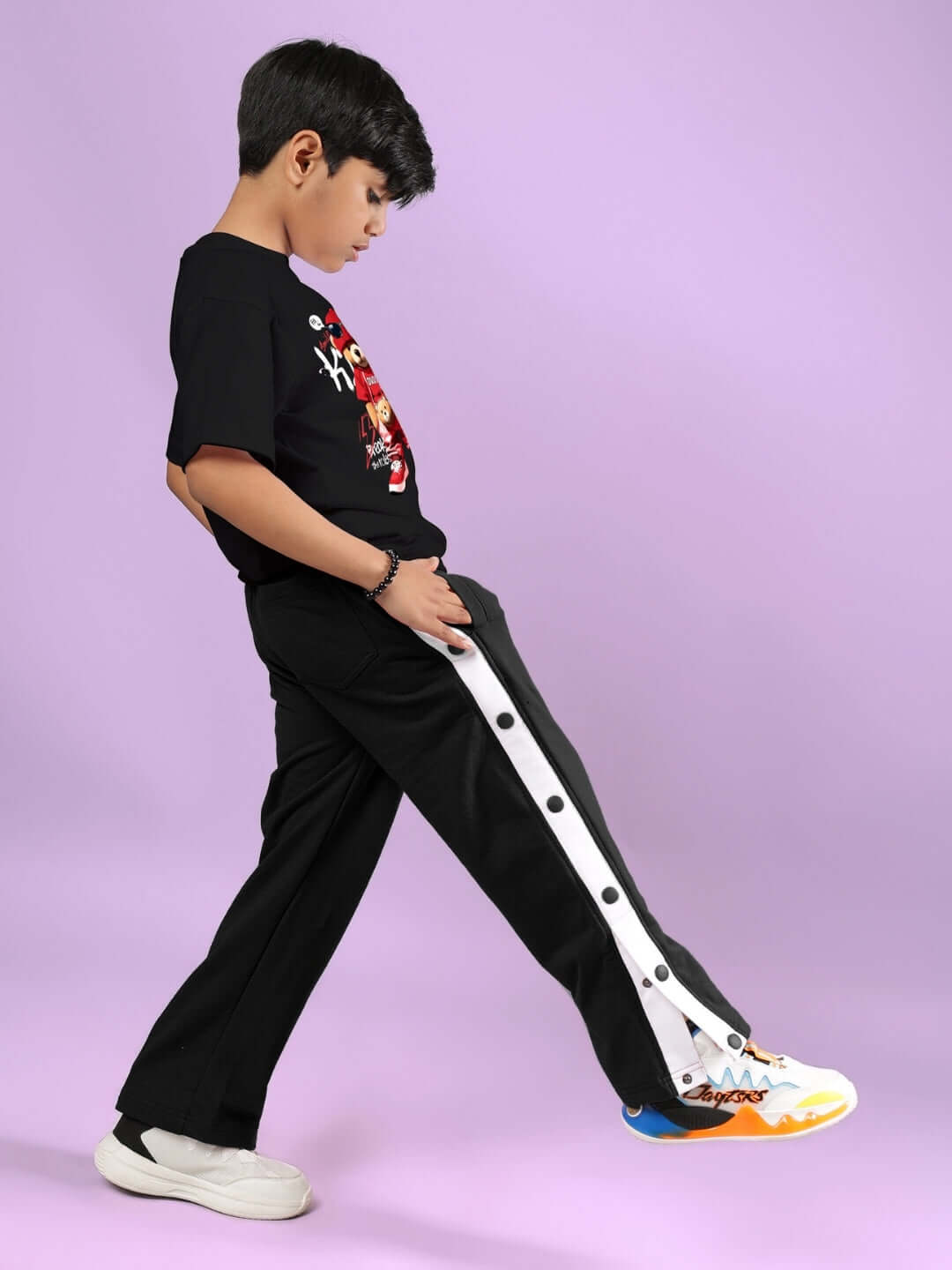 Child wearing HIP HOP TEDDY T-SHIRT FOR BOYS & GIRLS BLACK, standing in trendy black pants, showcasing streetwear style.