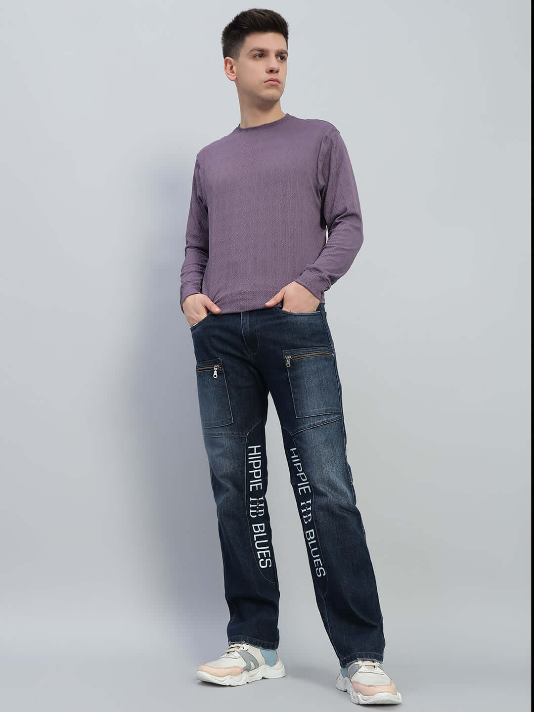 Man wearing Hippie Blue regular fit denim jeans with text detail, paired with a purple long-sleeve shirt and white sneakers.