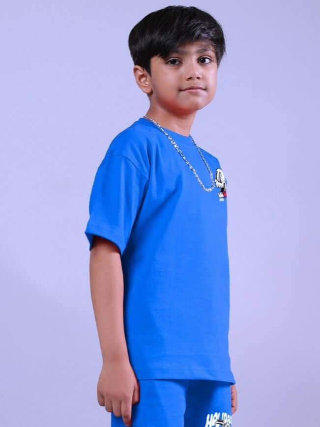 Child wearing HOLIDAY TIME RIDER PRINT T-SHIRT FOR BOYS AND GIRLS BLUE, standing against lavender background.