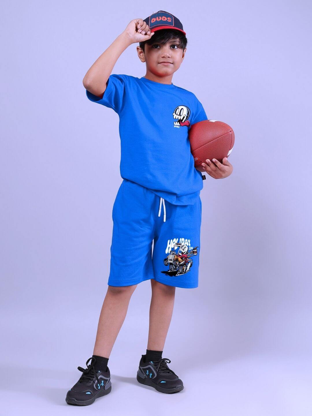 Child wearing HOLIDAY TIME RIDER PRINT SHORTS FOR BOYS AND GIRLS BLUE and holding a football.