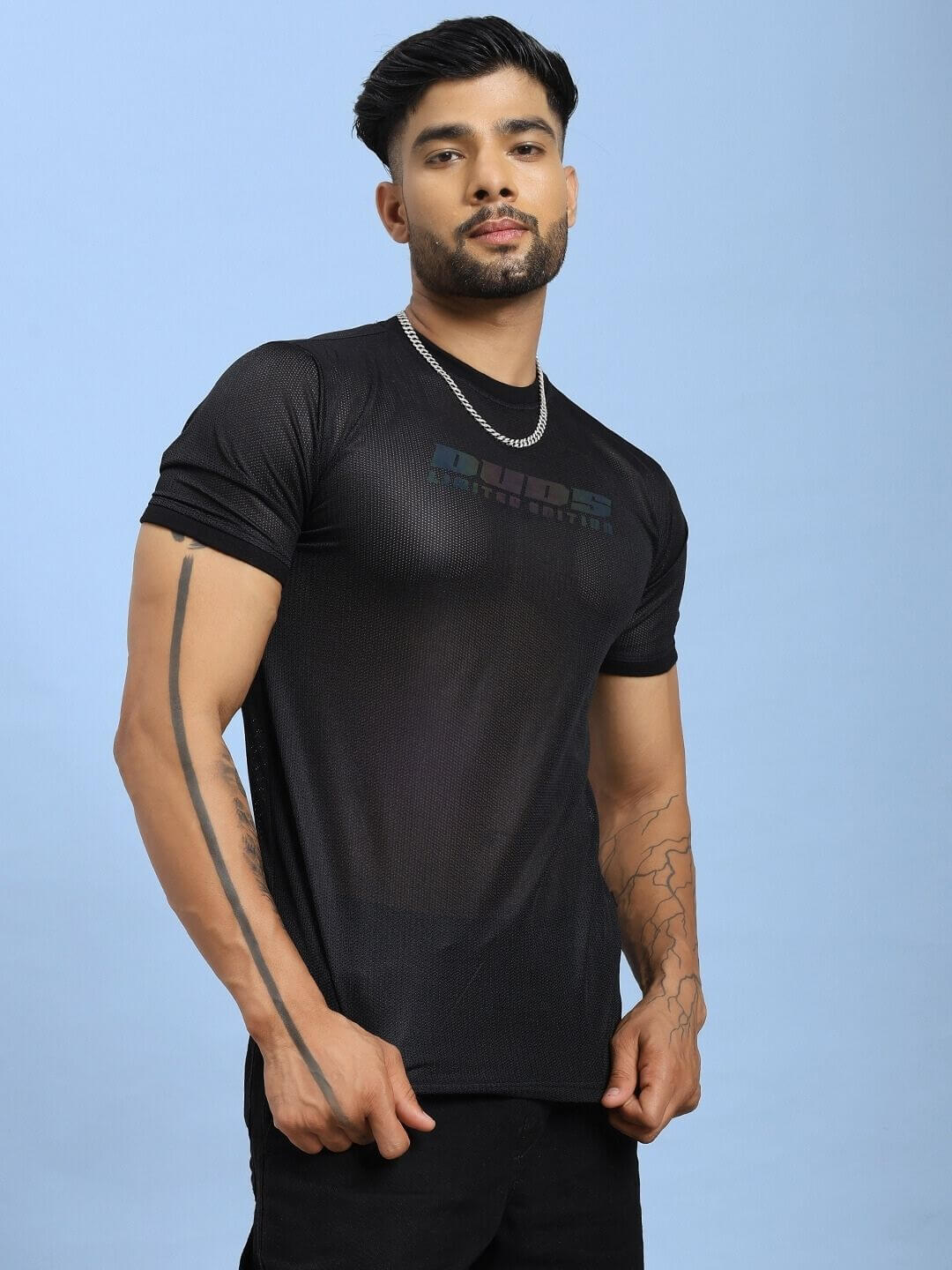 Man wearing HOLO BLACK MESH REGULAR FIT T-SHIRT BLACK with mesh panel design, posing against blue background.