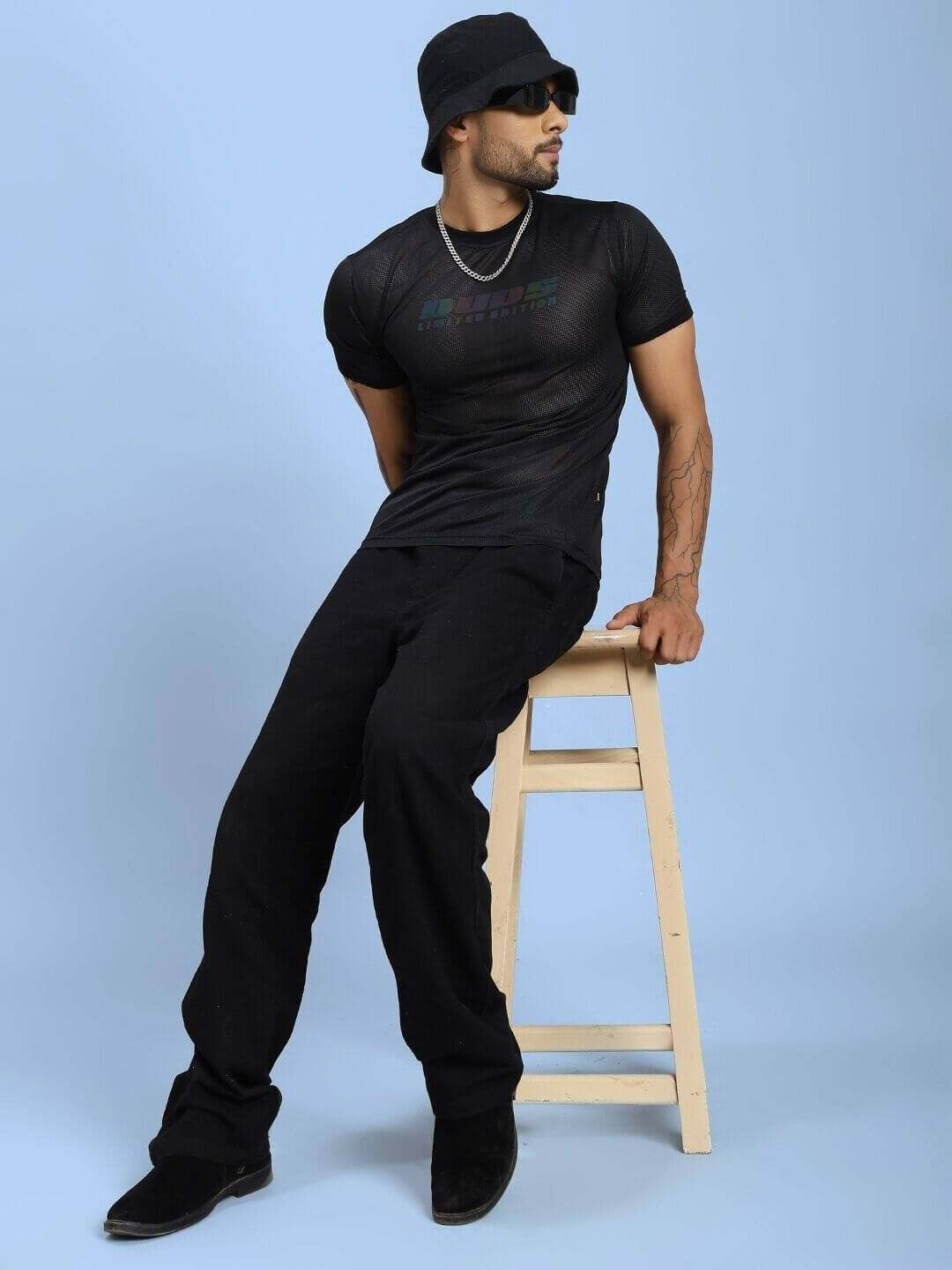 Model wearing HOLO BLACK MESH REGULAR FIT T-SHIRT BLACK, featuring mesh panel design for breathability and style, seated on a stool.
