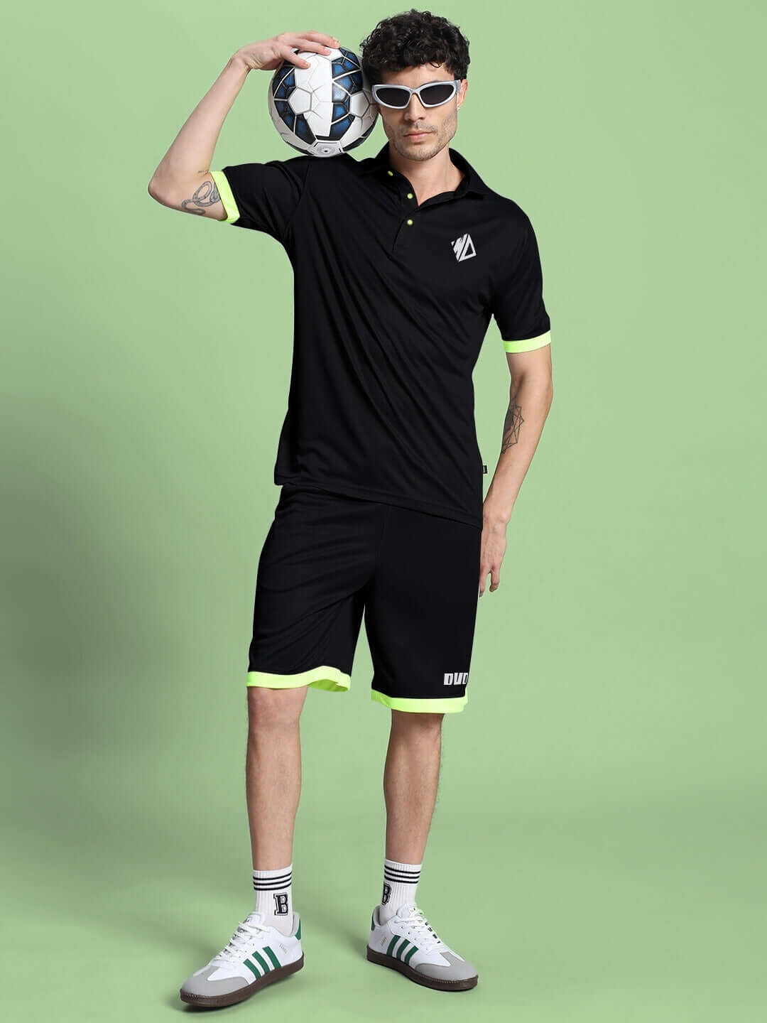 Person wearing the HOOKUP REFLECTOR SUMMER CO-ORD SET BLACK with sunglasses and holding a soccer ball against a green background.