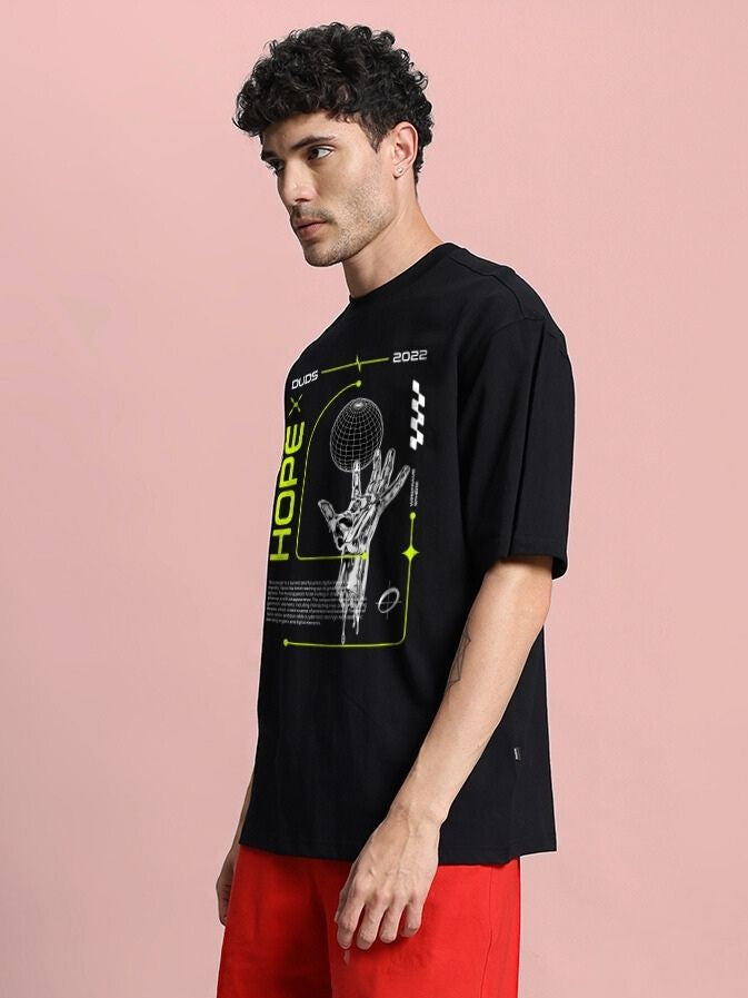 Man wearing HOPE PRINTED OVERSIZED T-SHIRT BLACK with graphic print, showcasing street style in a casual setting.
