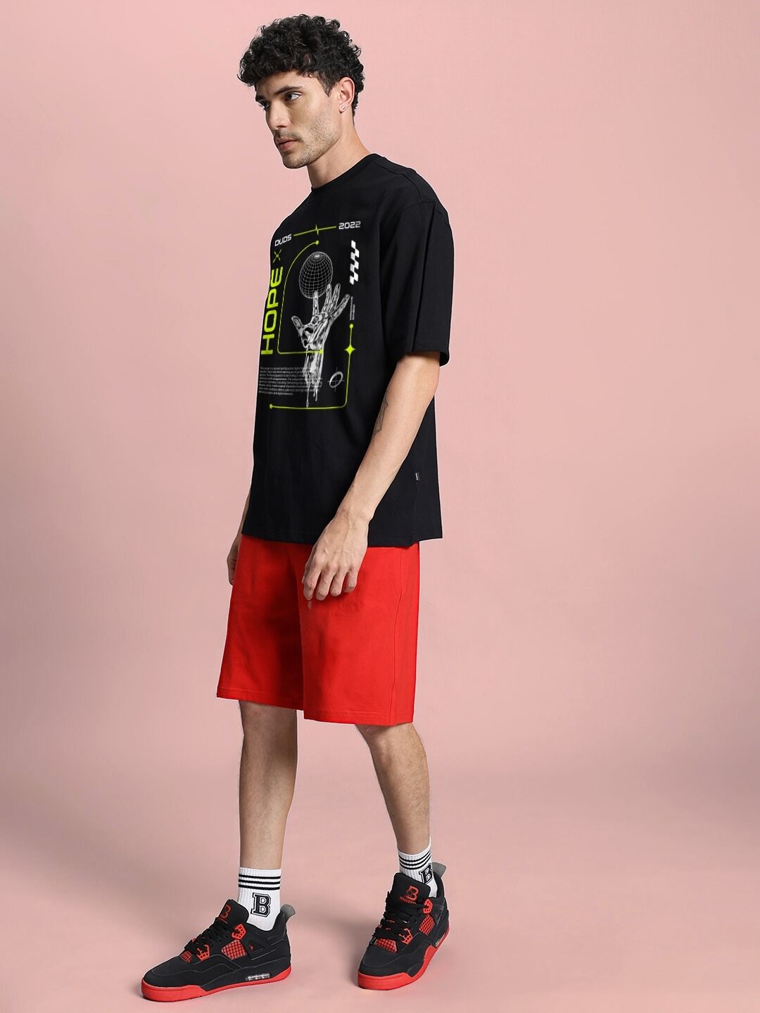 Man wearing HOPE PRINTED OVERSIZED CO-ORD SET BLACK RED with bold graphic tee and red shorts, showcasing trendy streetwear style.