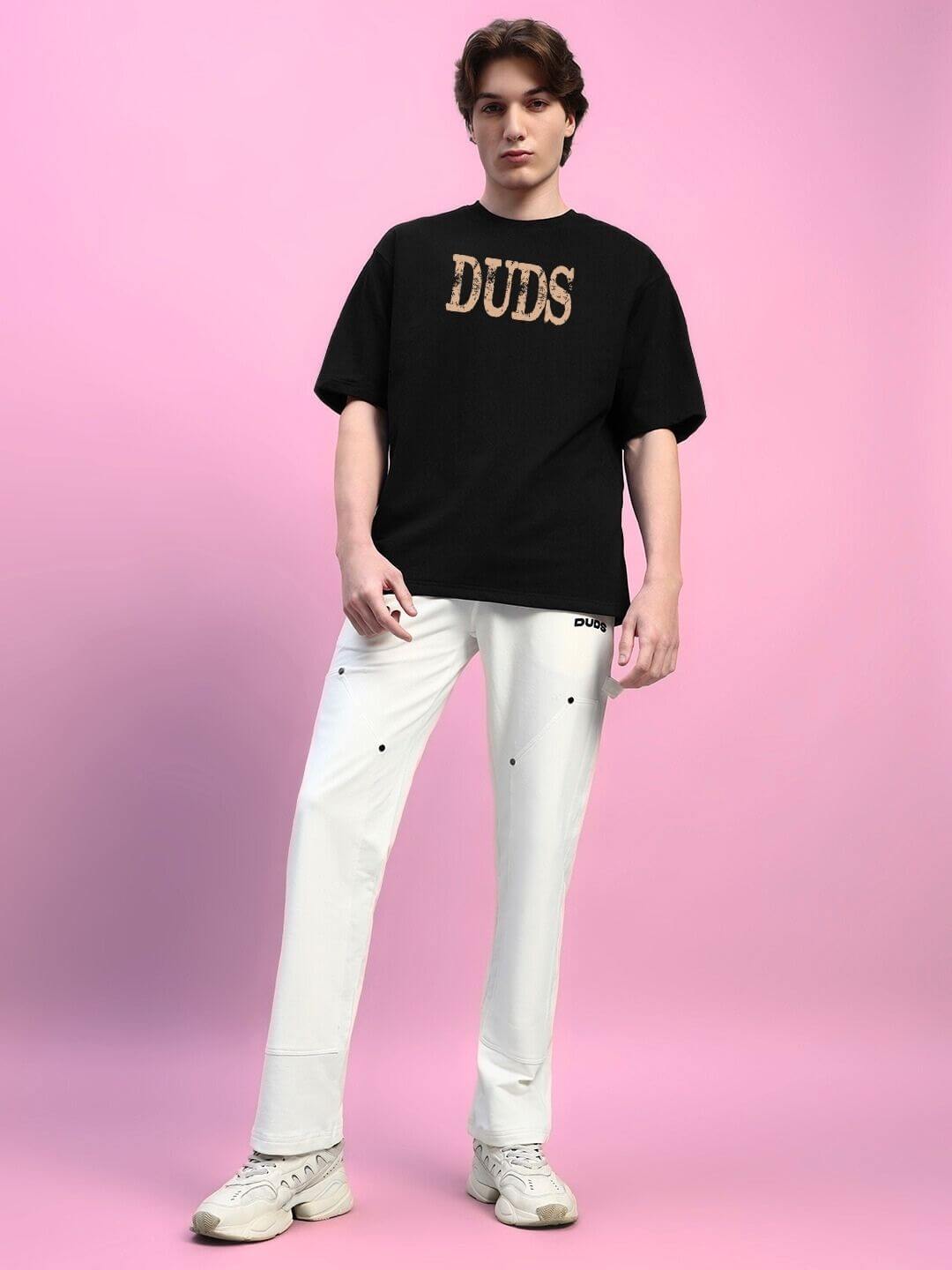 Model wearing black HORNED FIGURE CREATIVE PRINT OVERSIZED T-SHIRT with white pants on pink background.